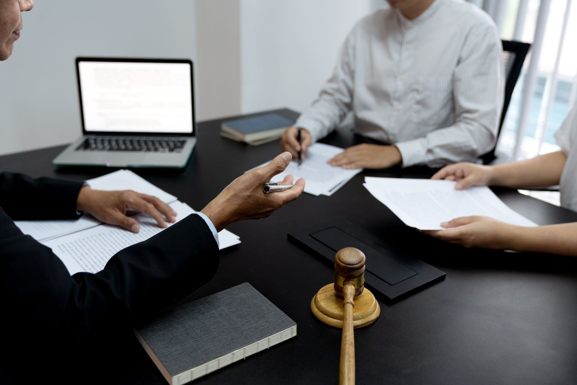 People in a business meeting exchanging documents across a conference table with a laptop and notebook.