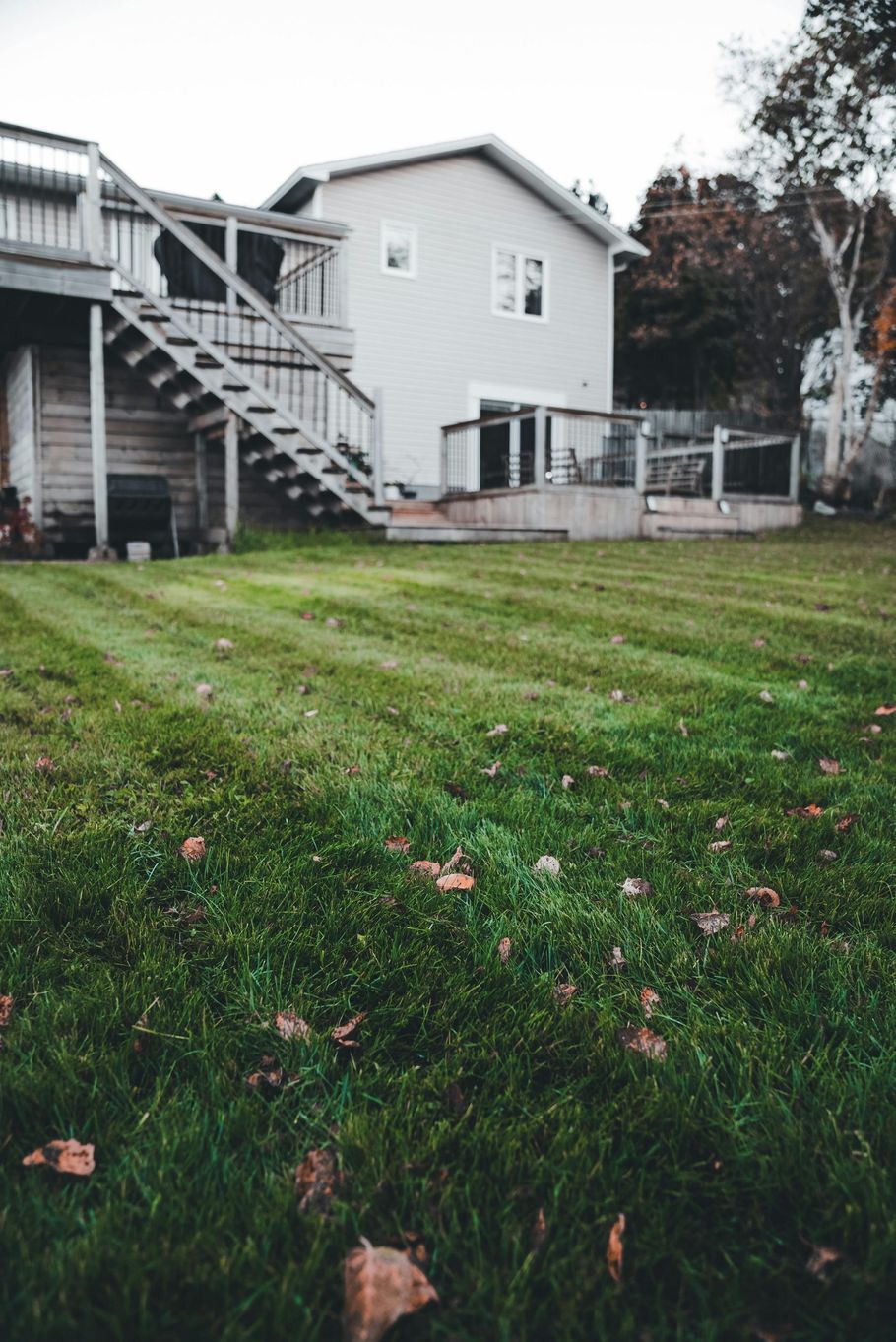 Backyard with green grass, a white house, and an exterior staircase on a cloudy day