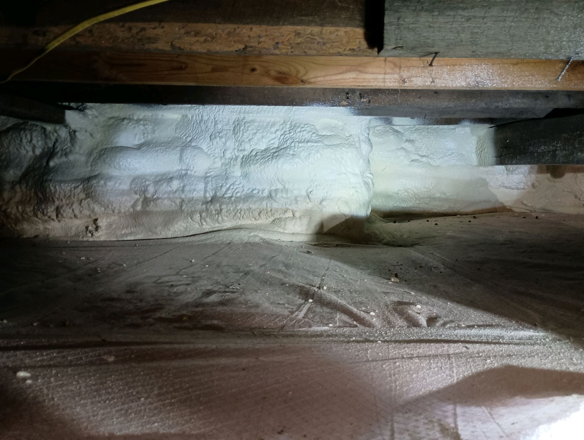 Spray foam insulation between wooden beams in a crawl space.