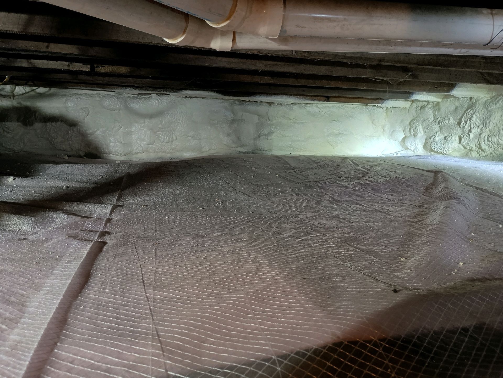 Under-house view showing insulation, netting, and pipes, likely for moisture control.