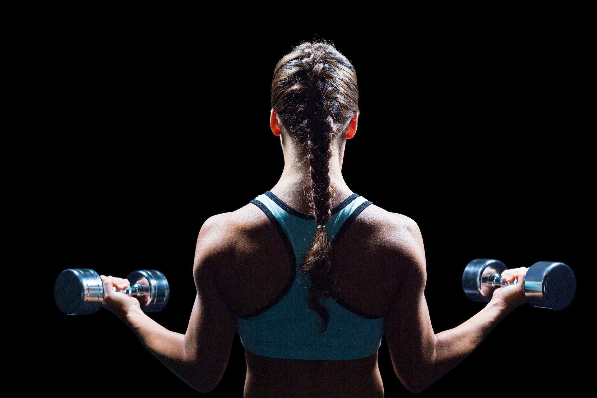A woman is lifting dumbbells in front of a black background.