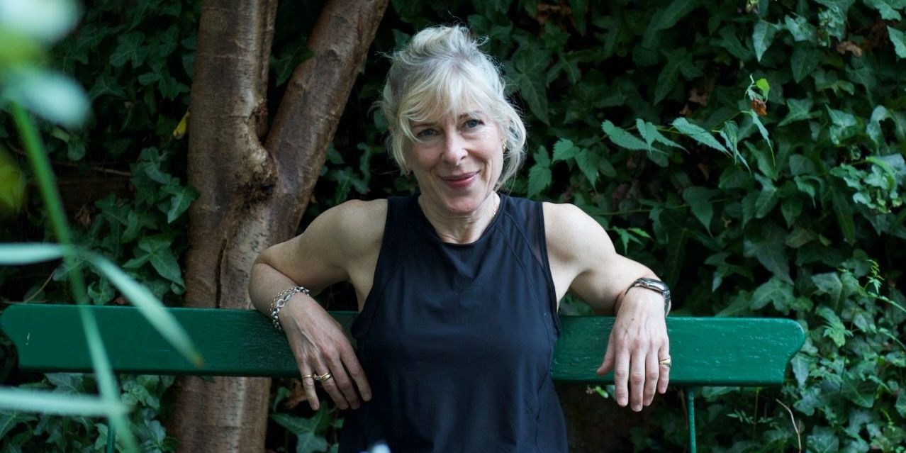 A woman is sitting on a green bench in front of a tree.