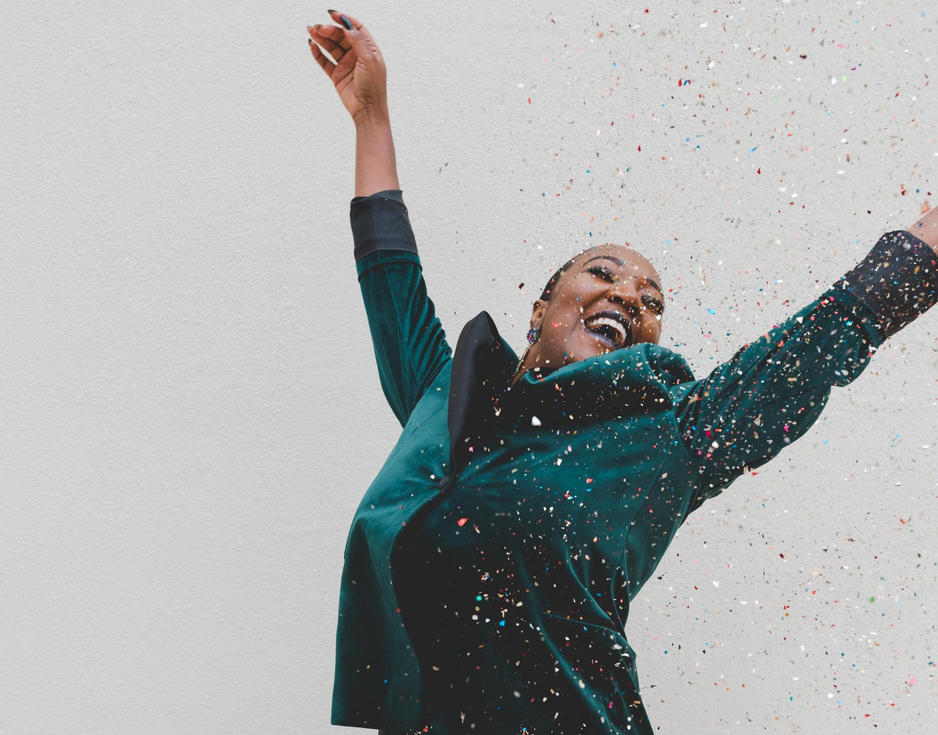A woman in a green jacket is throwing confetti in the air.