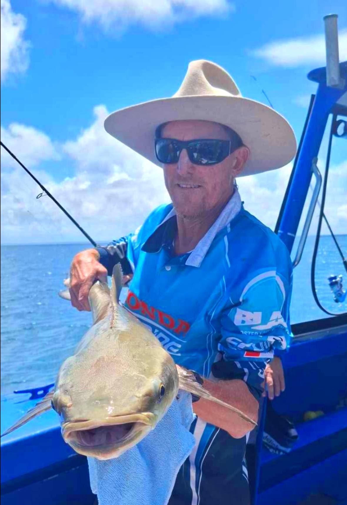 A Man Wearing a Hat and Sunglasses is Holding a Fish on a Boat — Whitsunday Fishing Charters In Airlie Beach, QLD