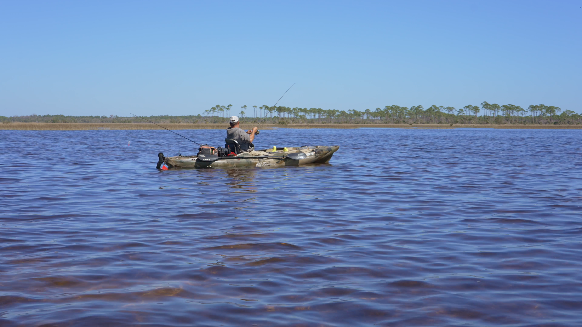 Person fishing from a small boat on a calm blue lake with a distant shoreline.