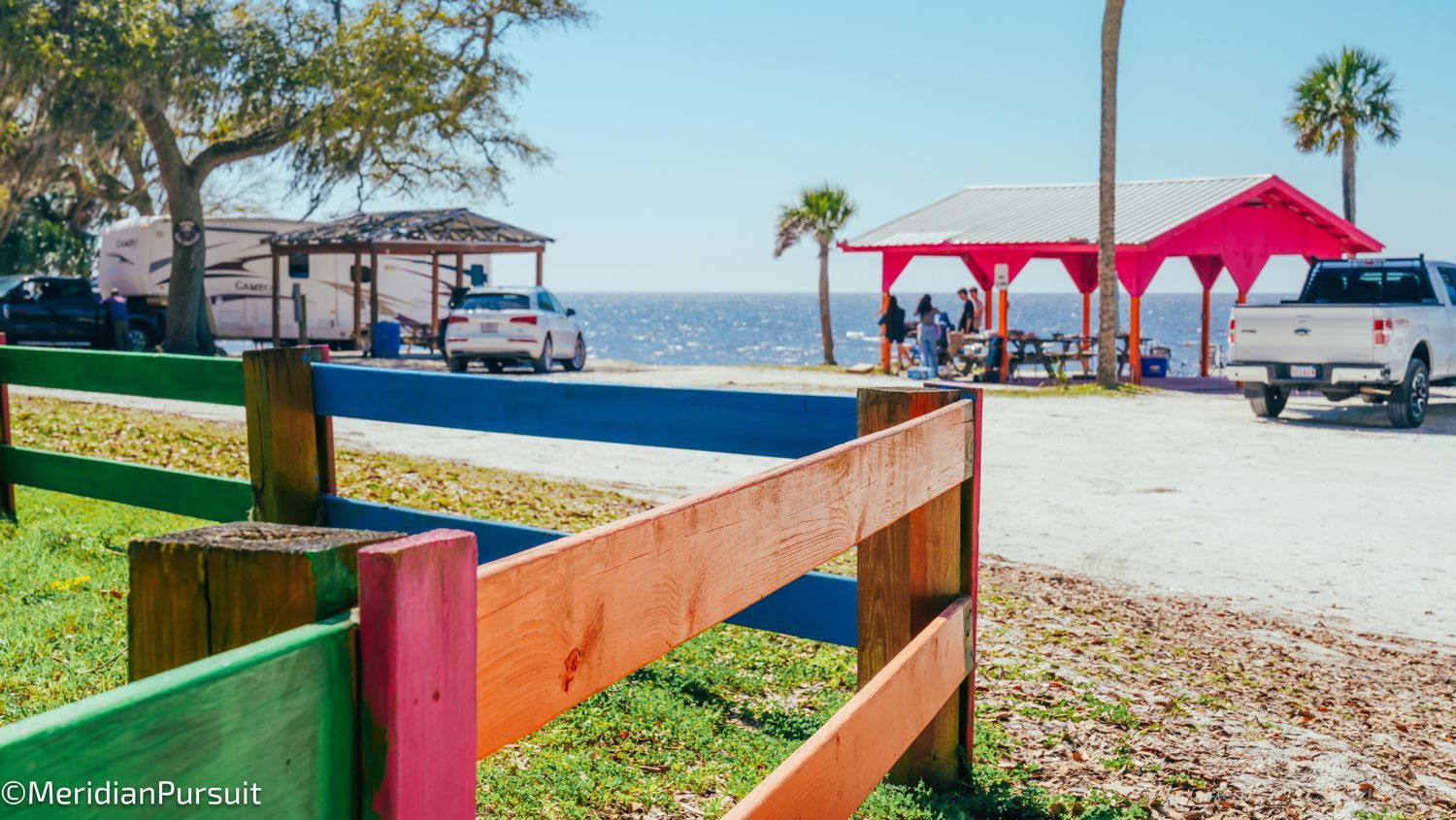 A colorful wooden fence surrounds a picnic area near the ocean.