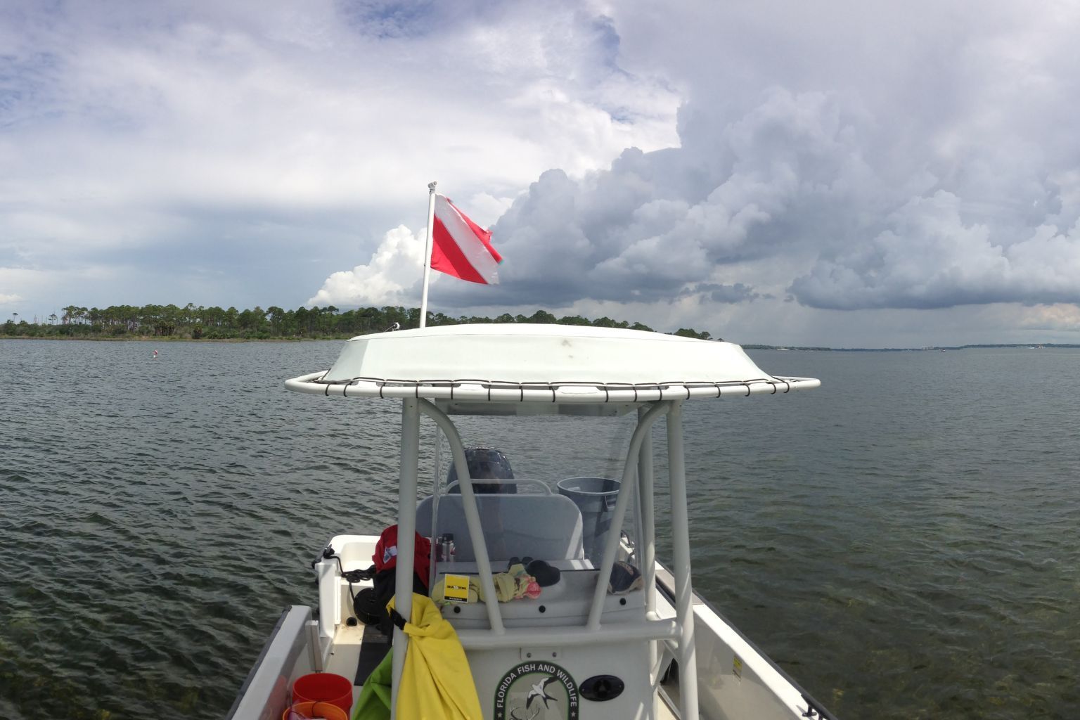 Kayaker in a yellow kayak on calm water, seen from a blue kayak near a tropical shoreline under cloudy sky