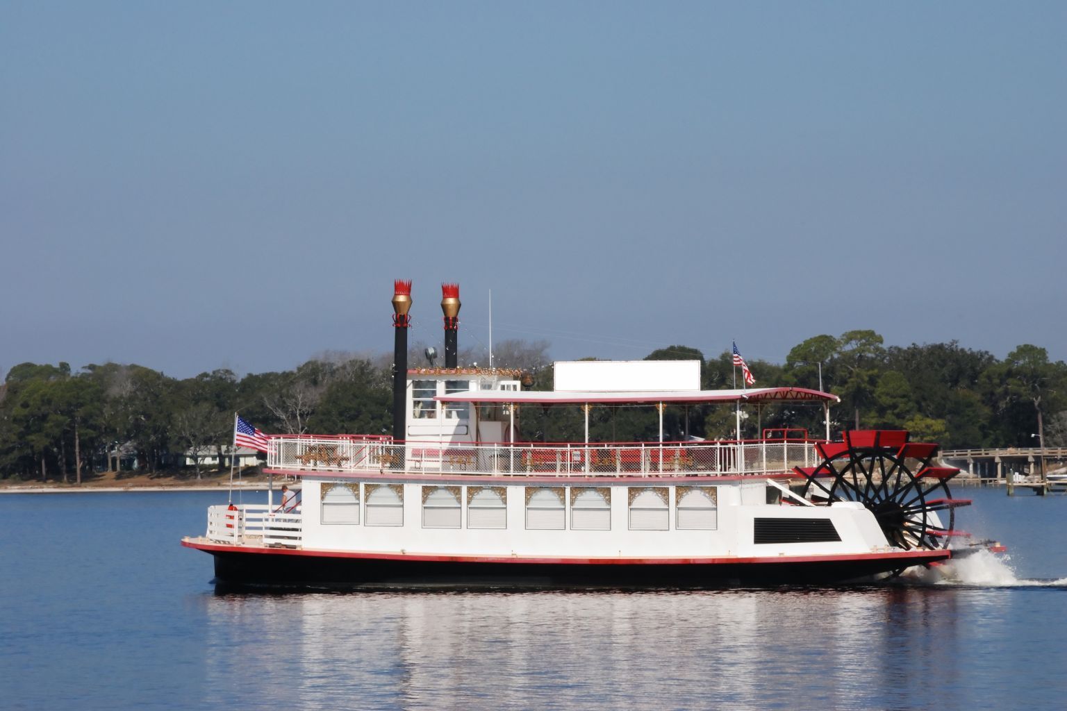 White riverboat with red paddlewheel on calm water under a clear sky