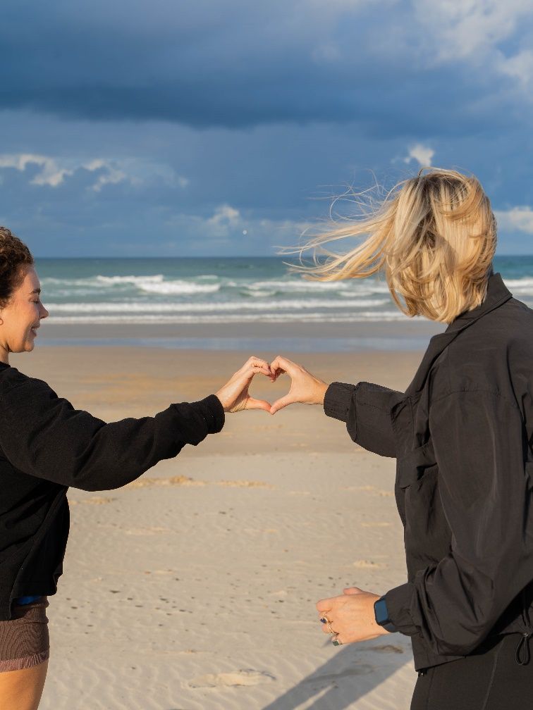 Two people forming a Heart-Centered shape with hands on the beach