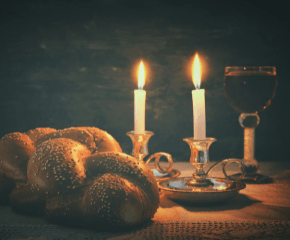 A photo of challah, lit Shabbat candles, and a kiddush cup 