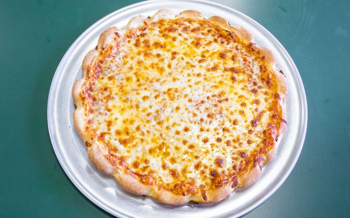 A round cheese pizza with a wavy, crusty edge sits on a metal tray against a dark green background.