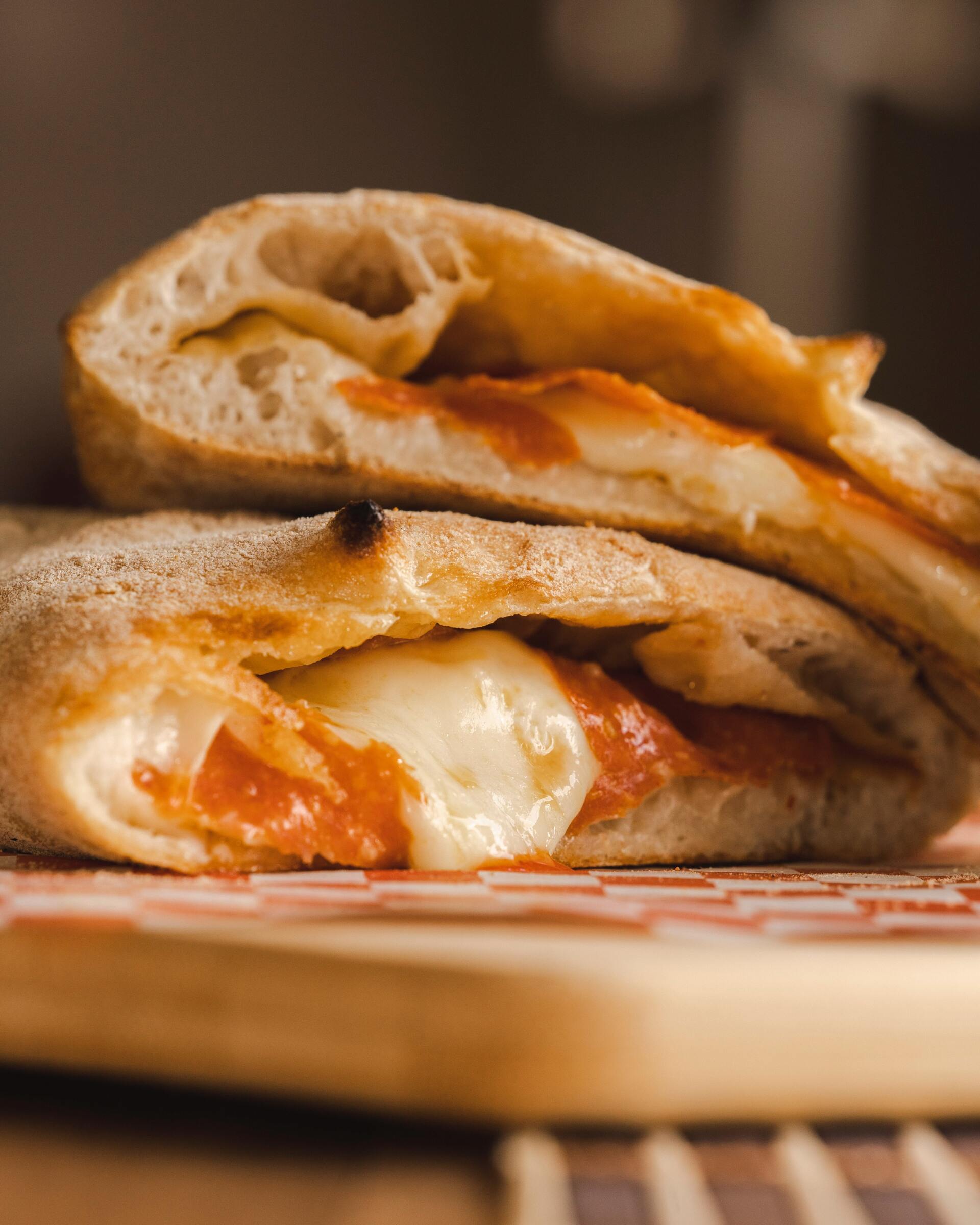 Two stacked calzones with melted mozzarella and red sauce peeking out from the golden-brown crust.