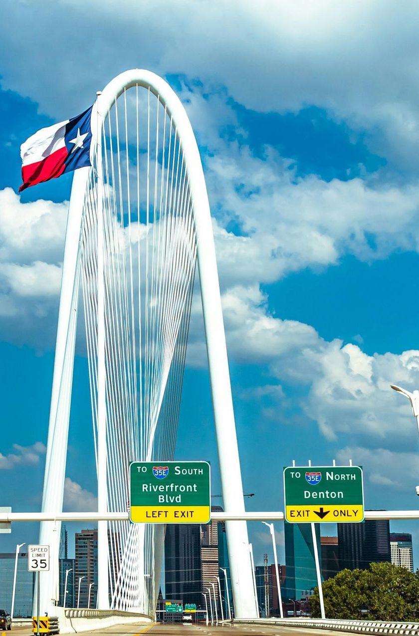 A texas flag is flying in front of a bridge in Denton, Tx