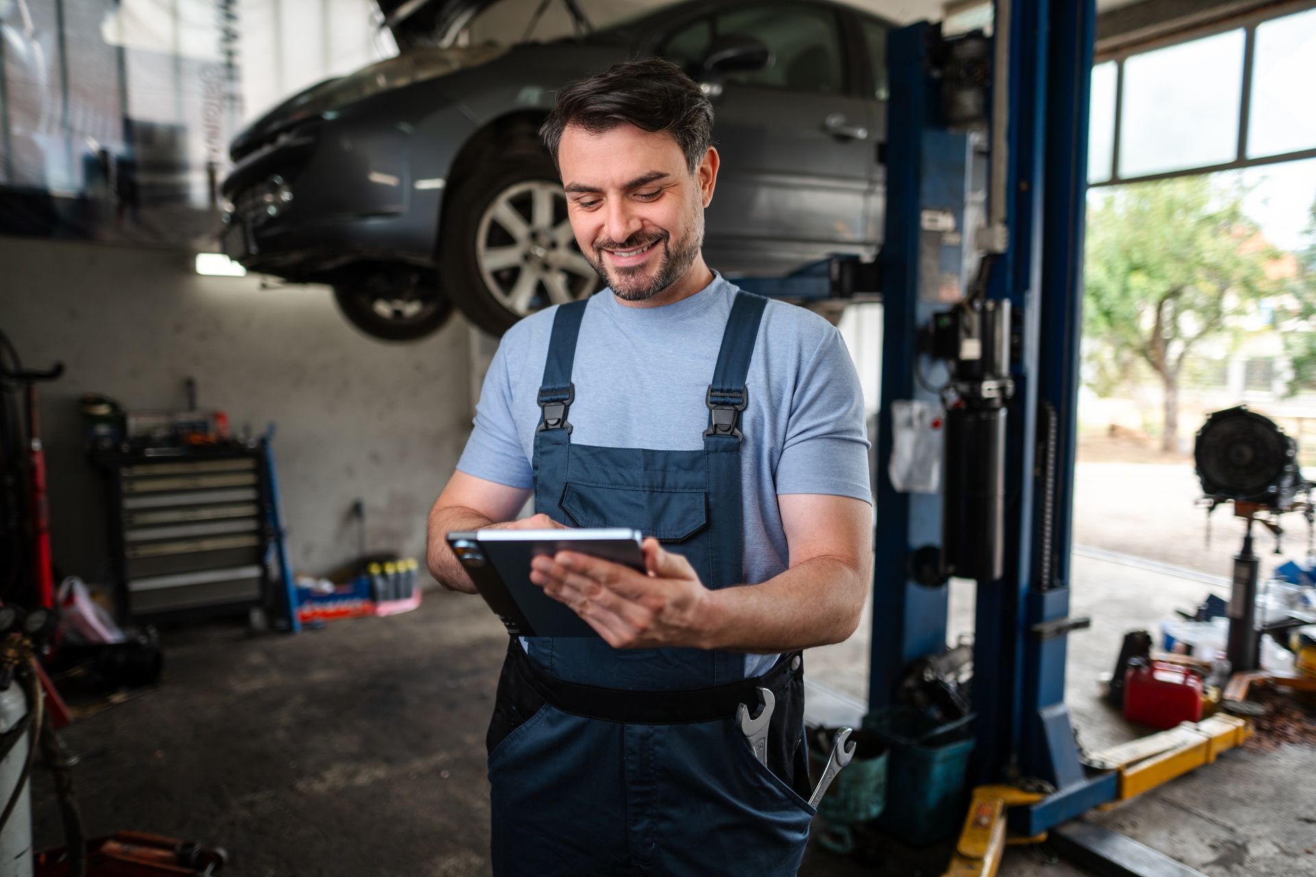 Mechanic using a tablet while working in an auto repair shop with a car on a lift.