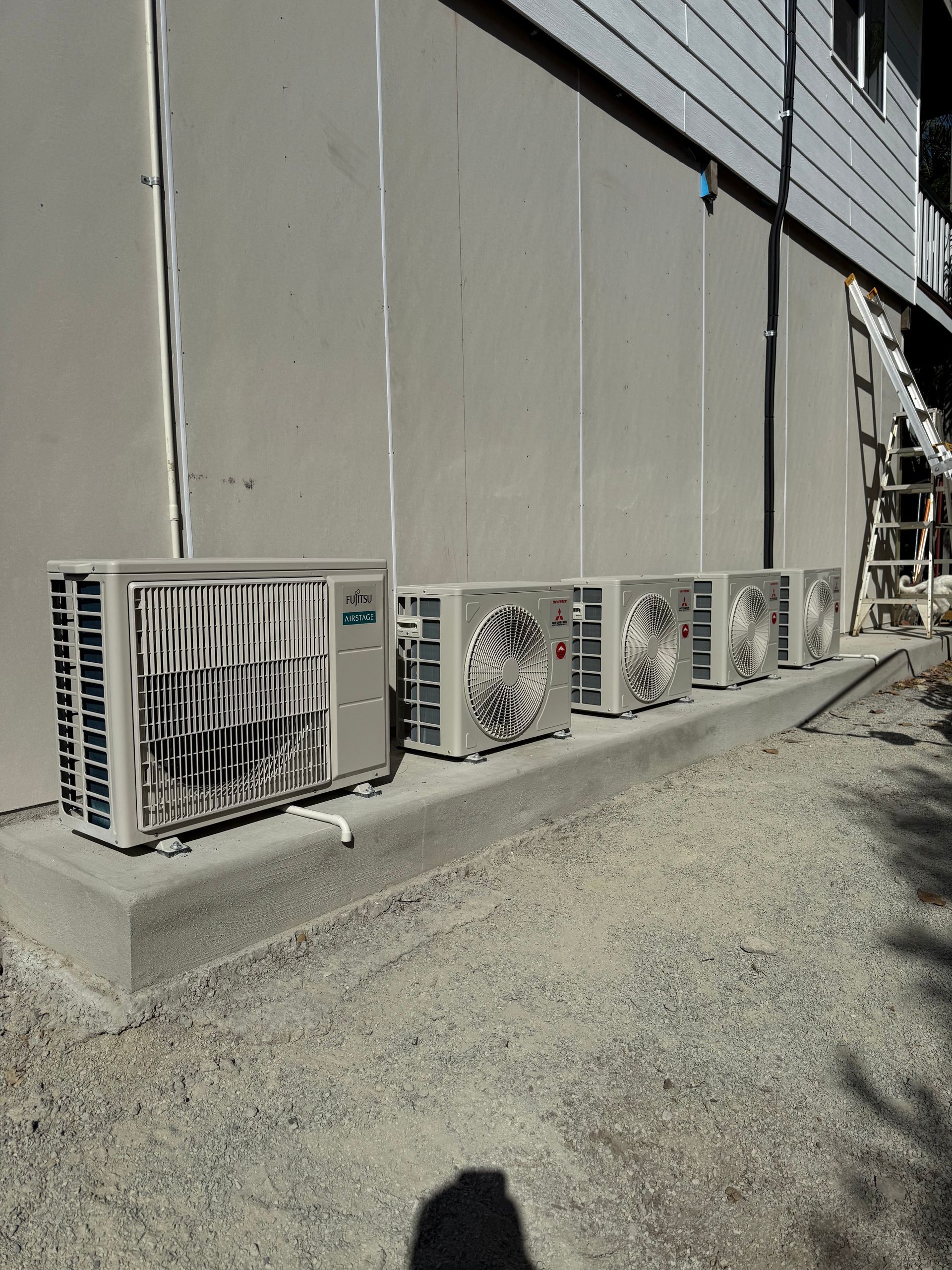 A row of five air conditioner units sitting on a concrete slab against the side of a building.