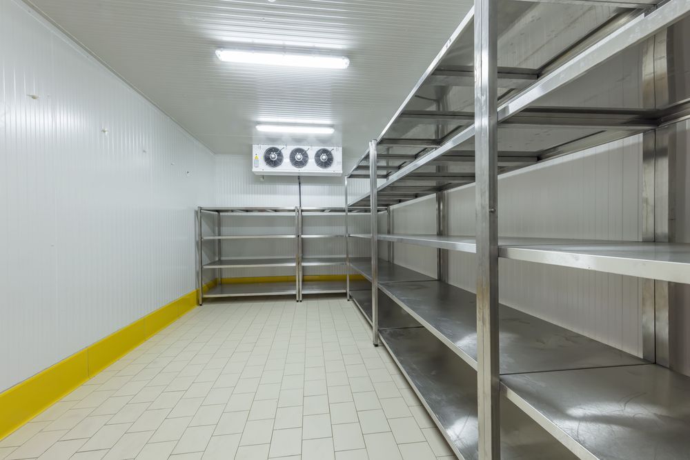A commercial walk-in refrigerator featuring stainless steel shelving, light-coloured tile floors, and a cooling unit.