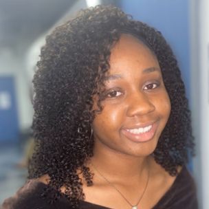 A woman with curly hair and a necklace is smiling for the camera.