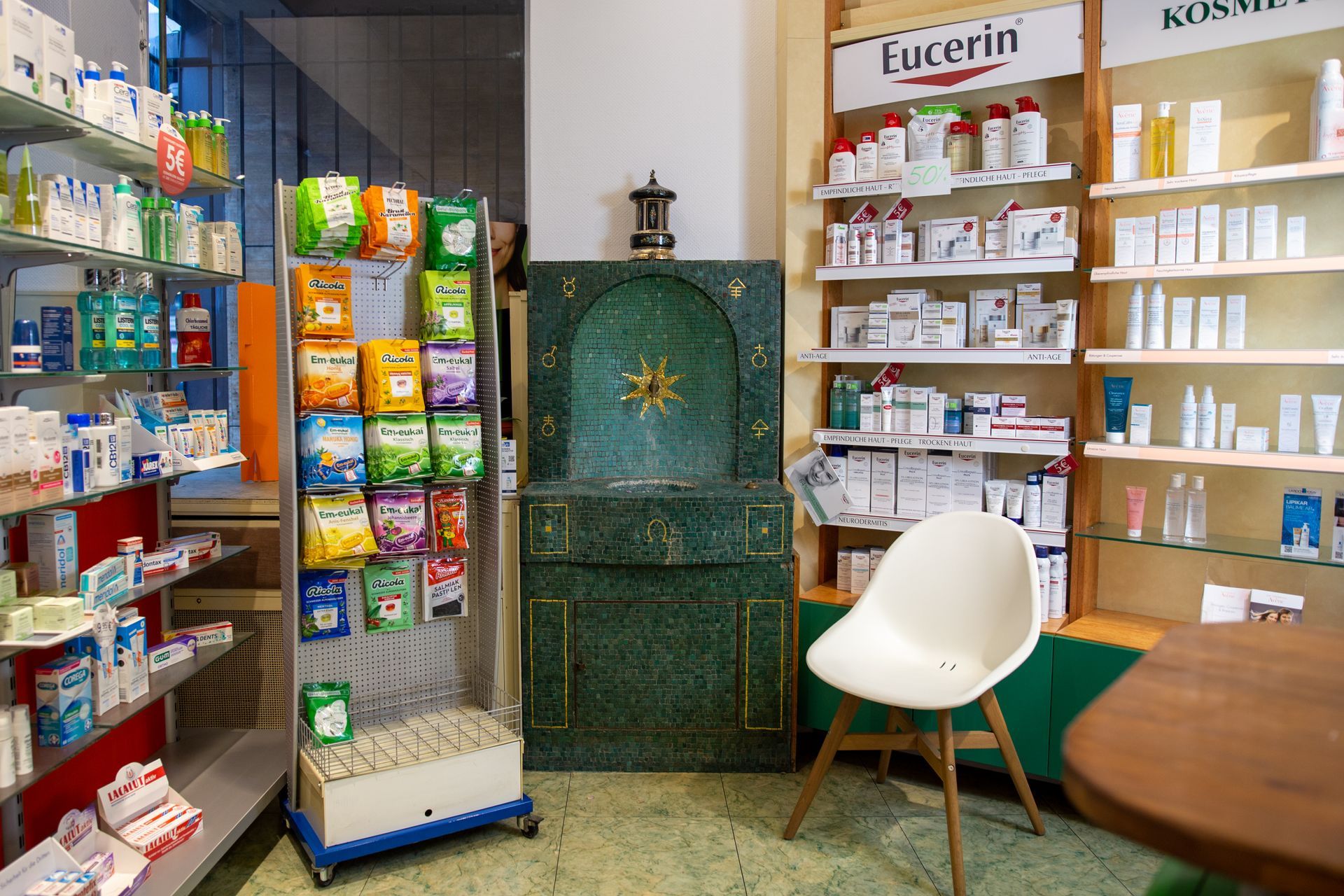 Das Interieur einer Apotheke mit Regalen voller Hautpflegeprodukte, einer Bodenauslage mit Snacks und einem grünen Dekorationsschrank.