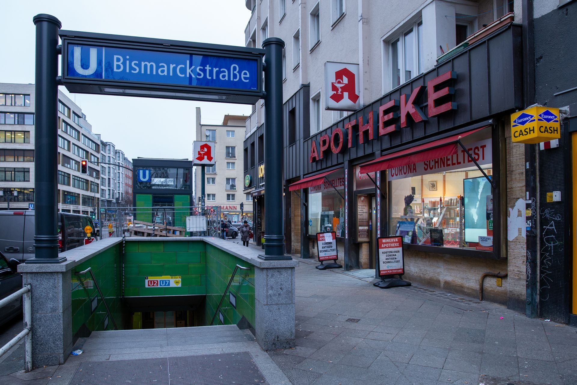 Ein Eingang zum U-Bahnhof Bismarckstraße neben einer Apotheke auf einem Berliner Bürgersteig.