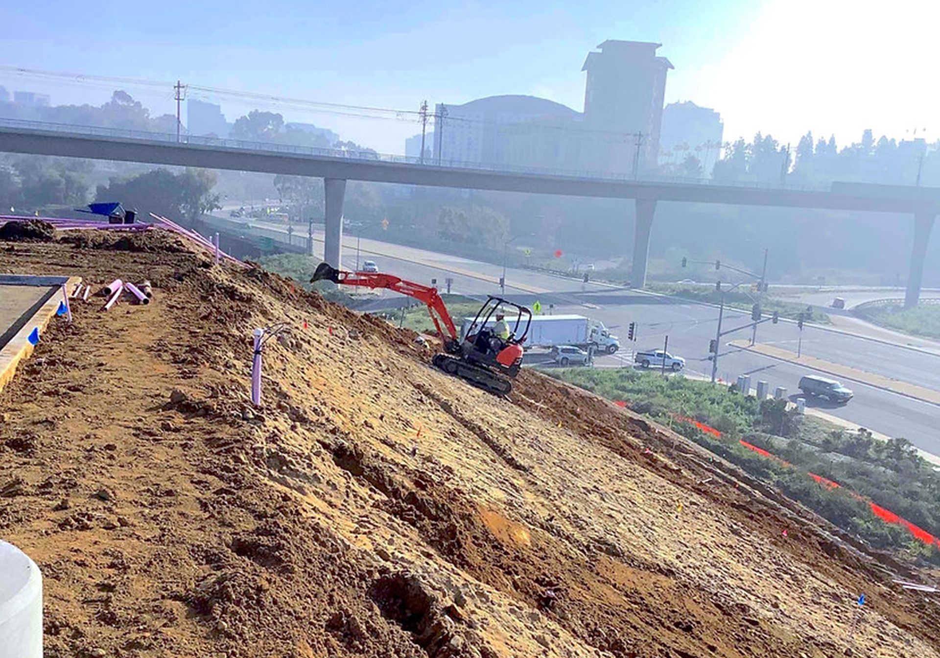 An excavator is working on a dirt hill next to a highway.