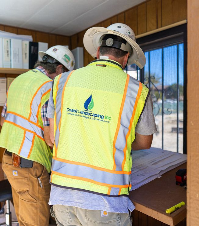 Two construction workers wearing safety vests and hard hats