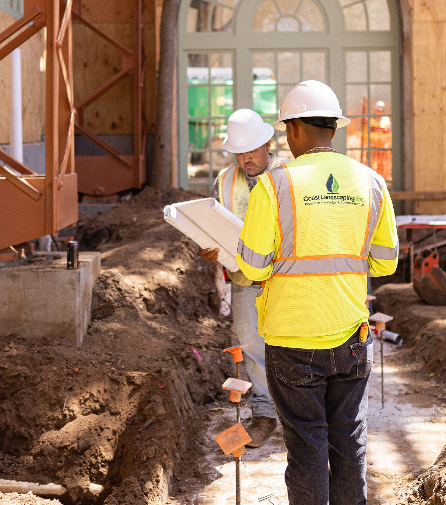 Two construction workers wearing hard hats and safety vests looking at a blueprint