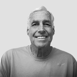 A black and white photo of an older man wearing a t-shirt and smiling.