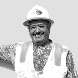 A man wearing a hard hat and safety vest is smiling in a black and white photo.