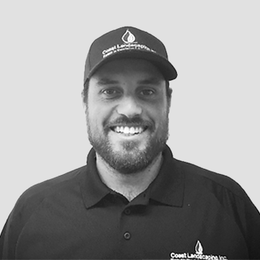 A man with a beard is wearing a hat and smiling in a black and white photo.