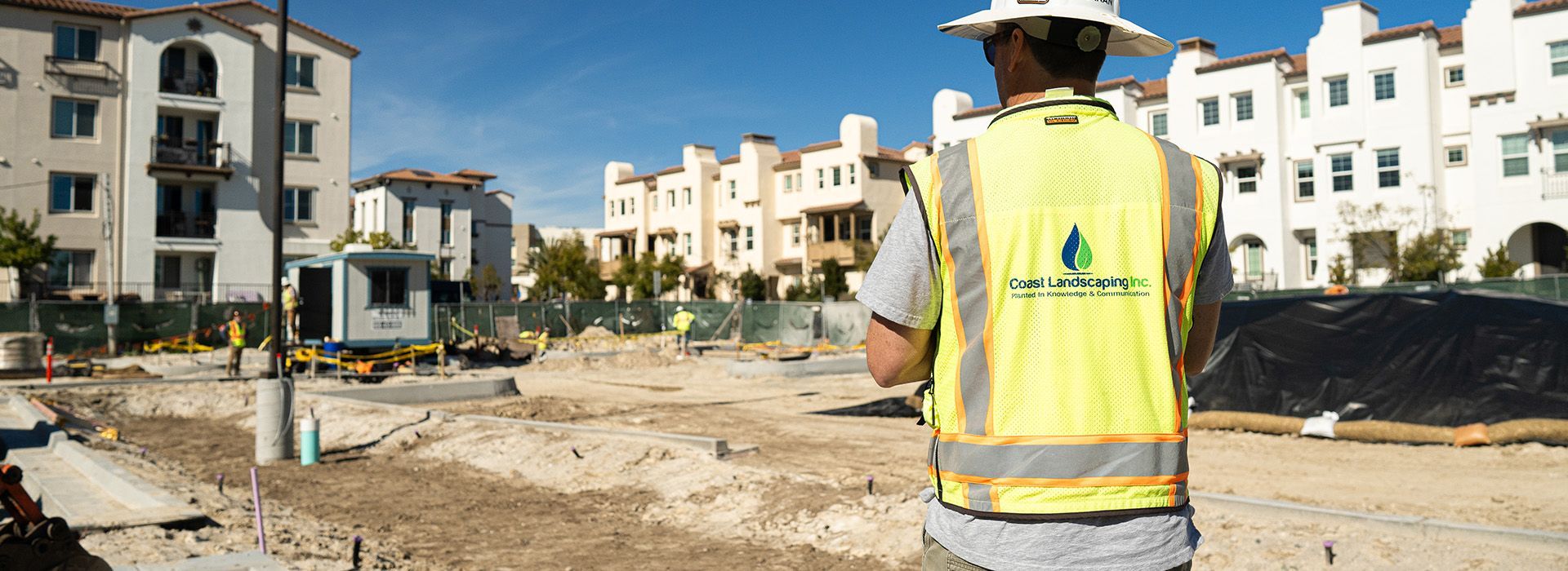 A man in a yellow vest and hard hat is standing in a construction site.