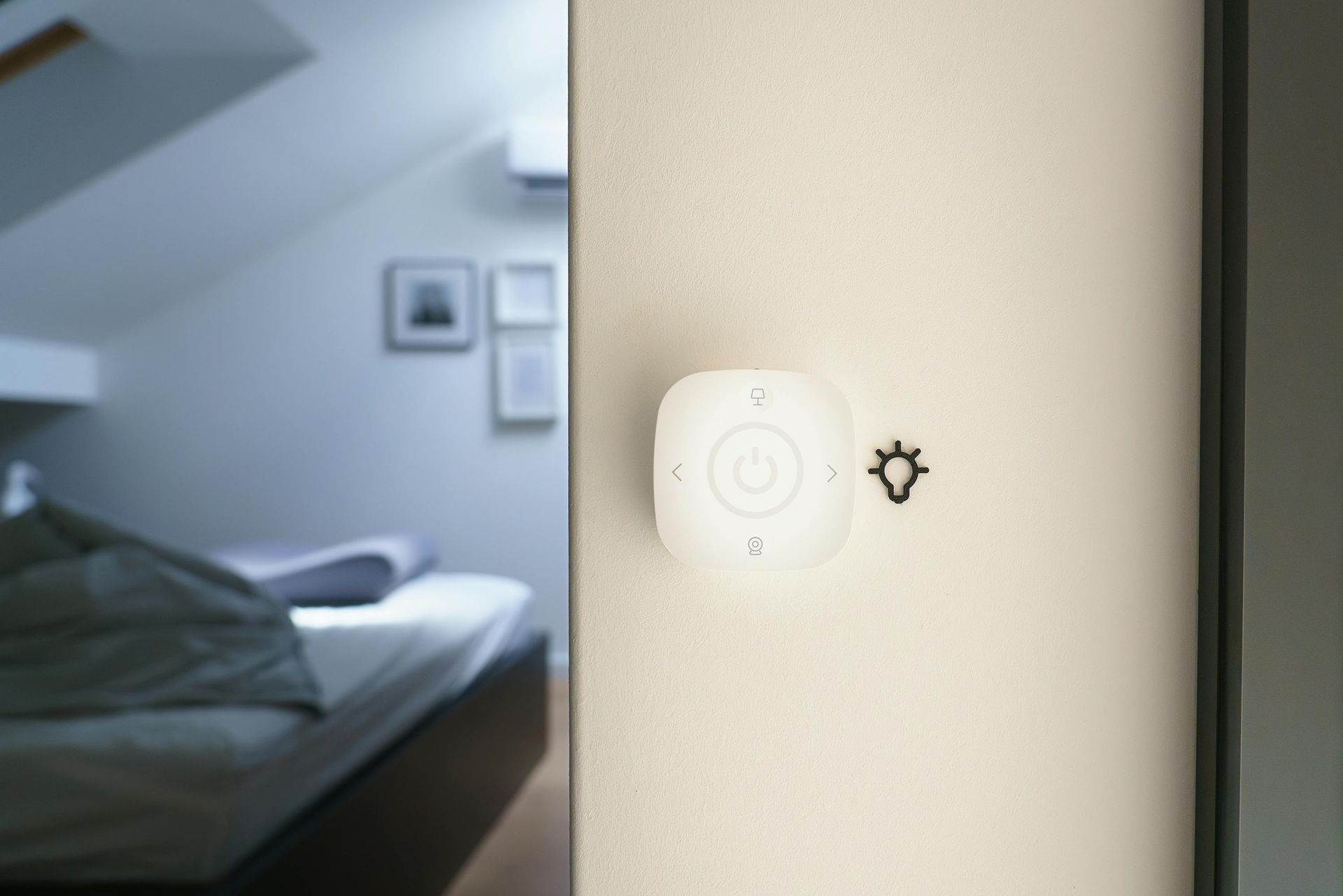 White wall-mounted light control with a lightbulb symbol next to it; bedroom visible in the background.