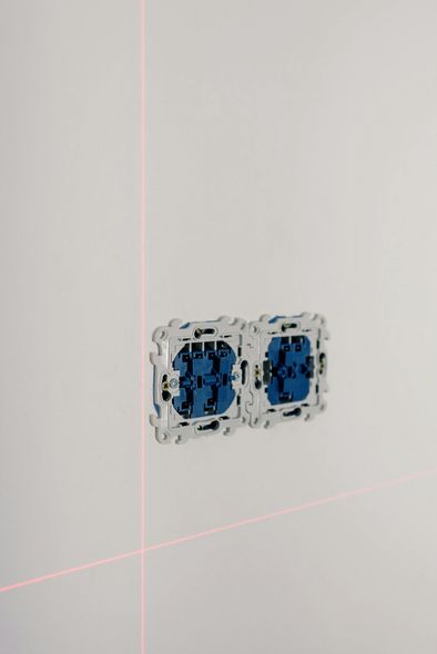 Two blue and white electrical outlets installed in a white wall with laser level lines.