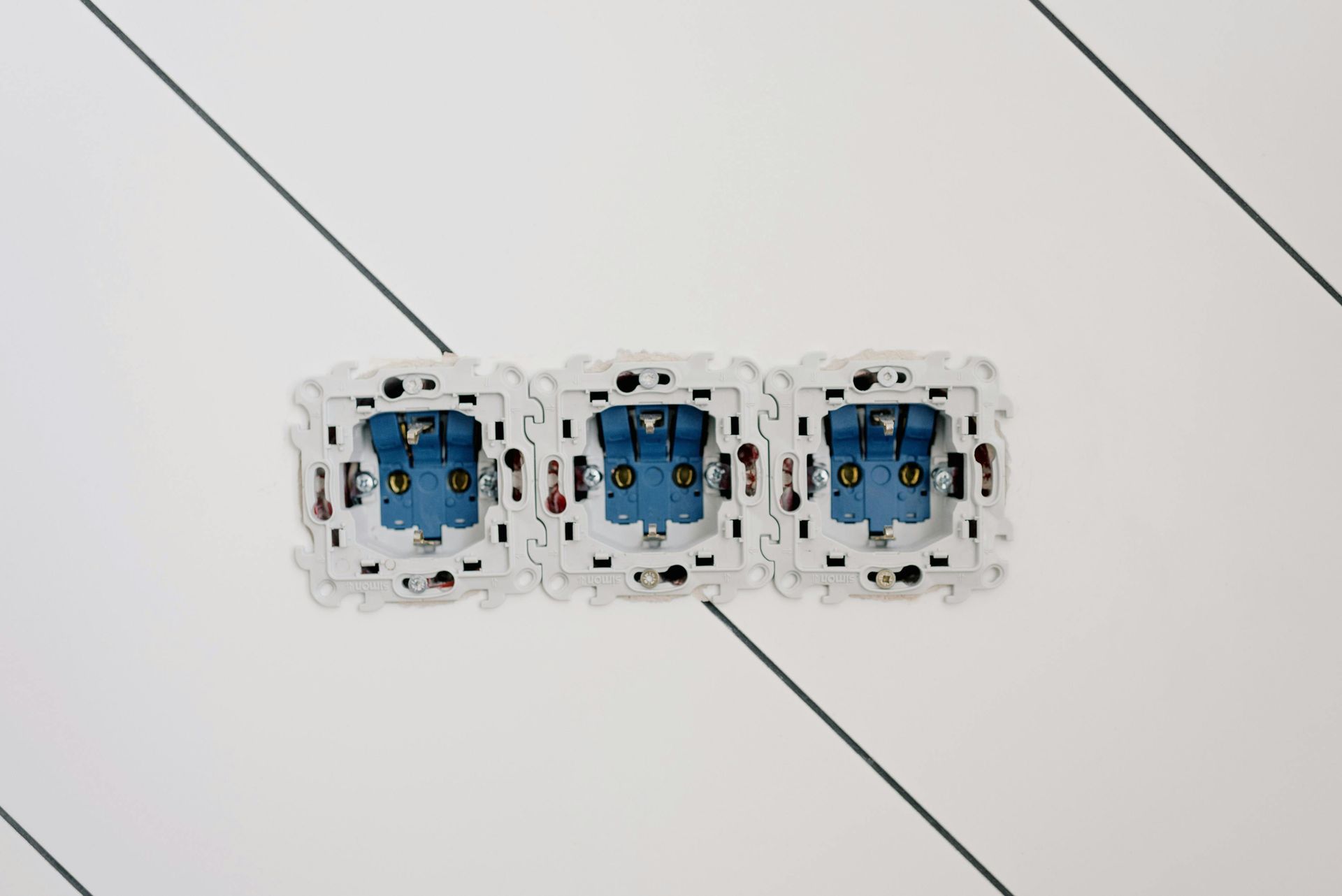 Three blue electrical outlets installed in a white wall with diagonal lines.