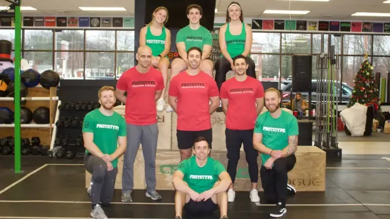 Fitness group posing in colorful shirts at a gym, standing and kneeling on a workout floor.