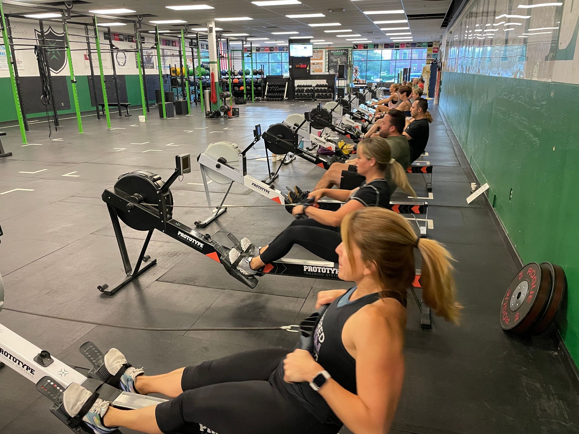 Group rowing workout in a gym, with people exercising on rowing machines in a bright studio.
