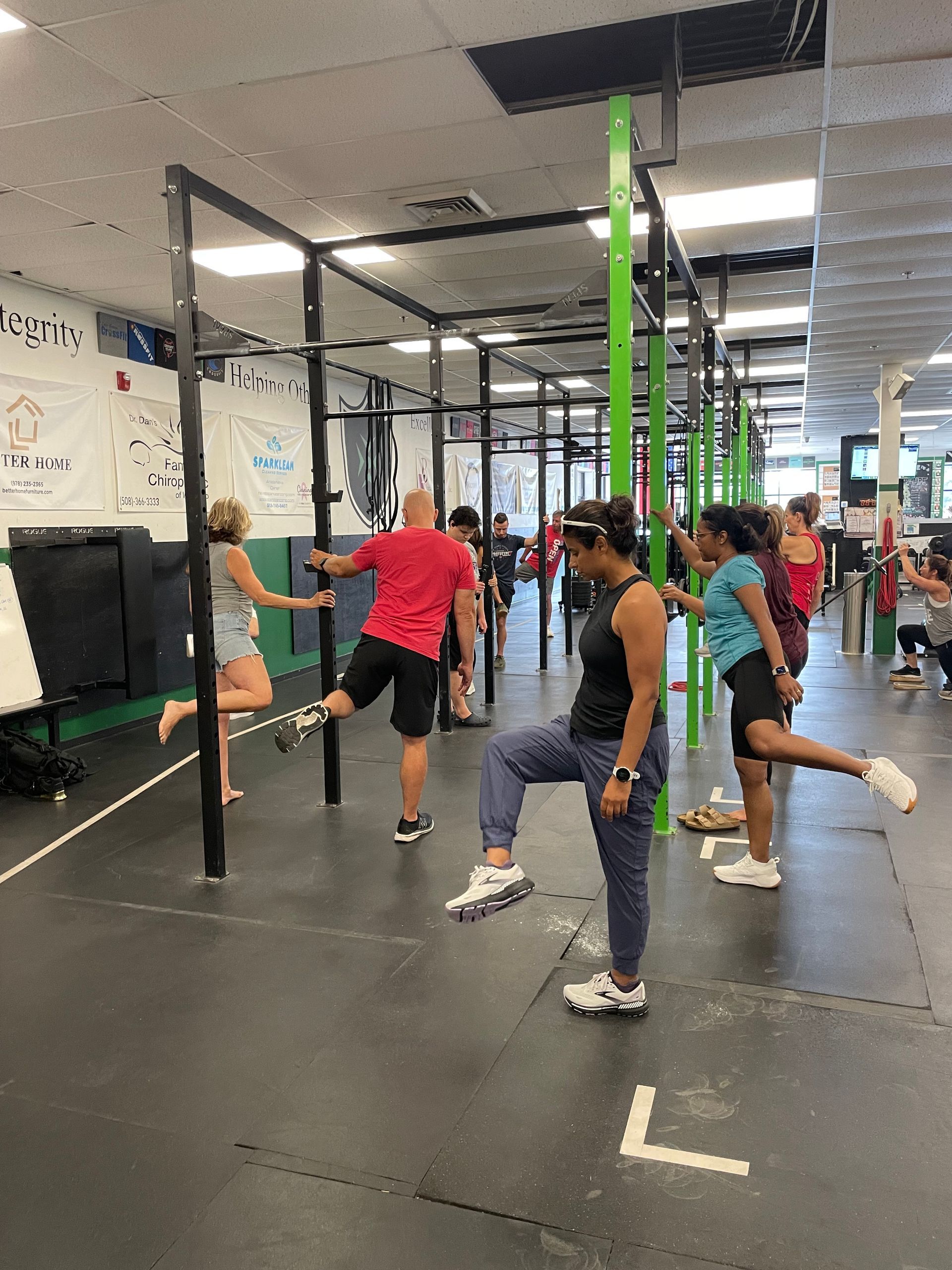 People exercising in a gym, doing leg stretches around pull-up bars.