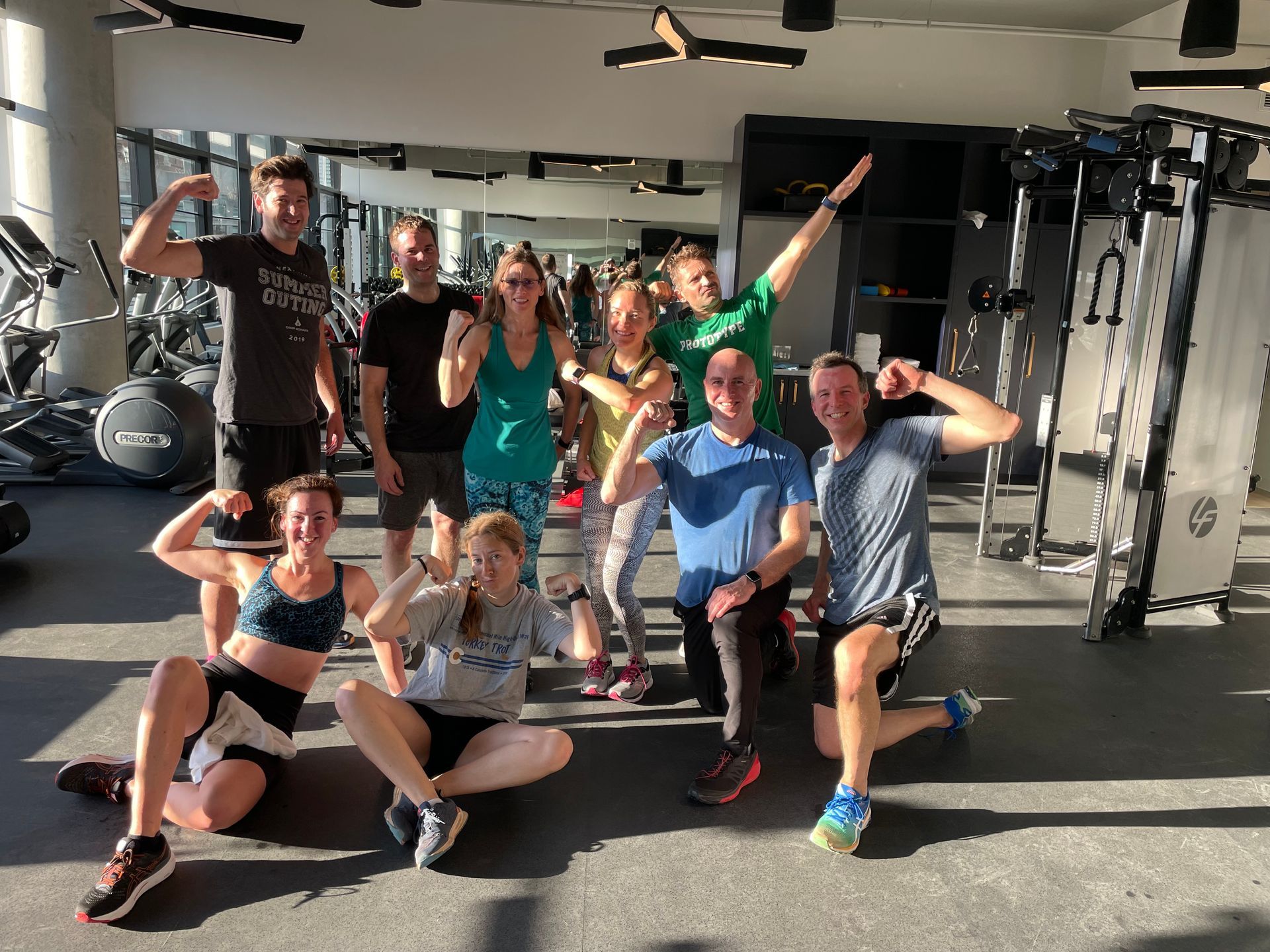 Group of people posing and flexing in a gym, smiling under bright lights.