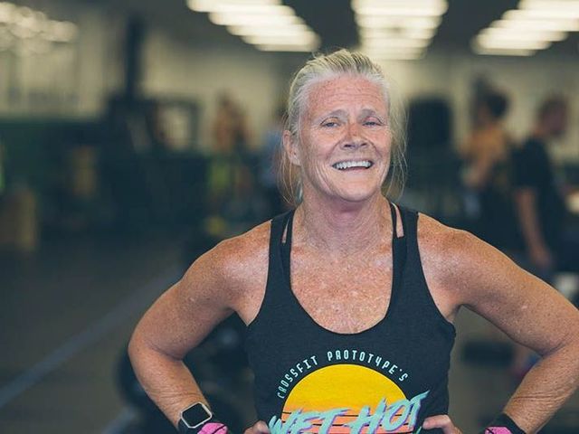 Smiling woman in a black tank top with hands on hips at a gym