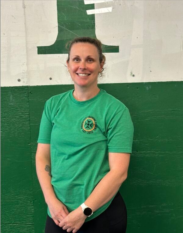 A woman in a green shirt is smiling in front of a green wall