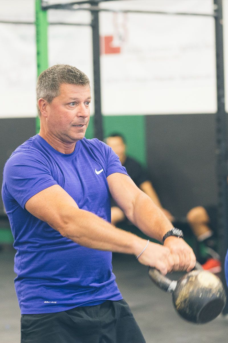 Man in a blue shirt swinging a kettlebell in a gym