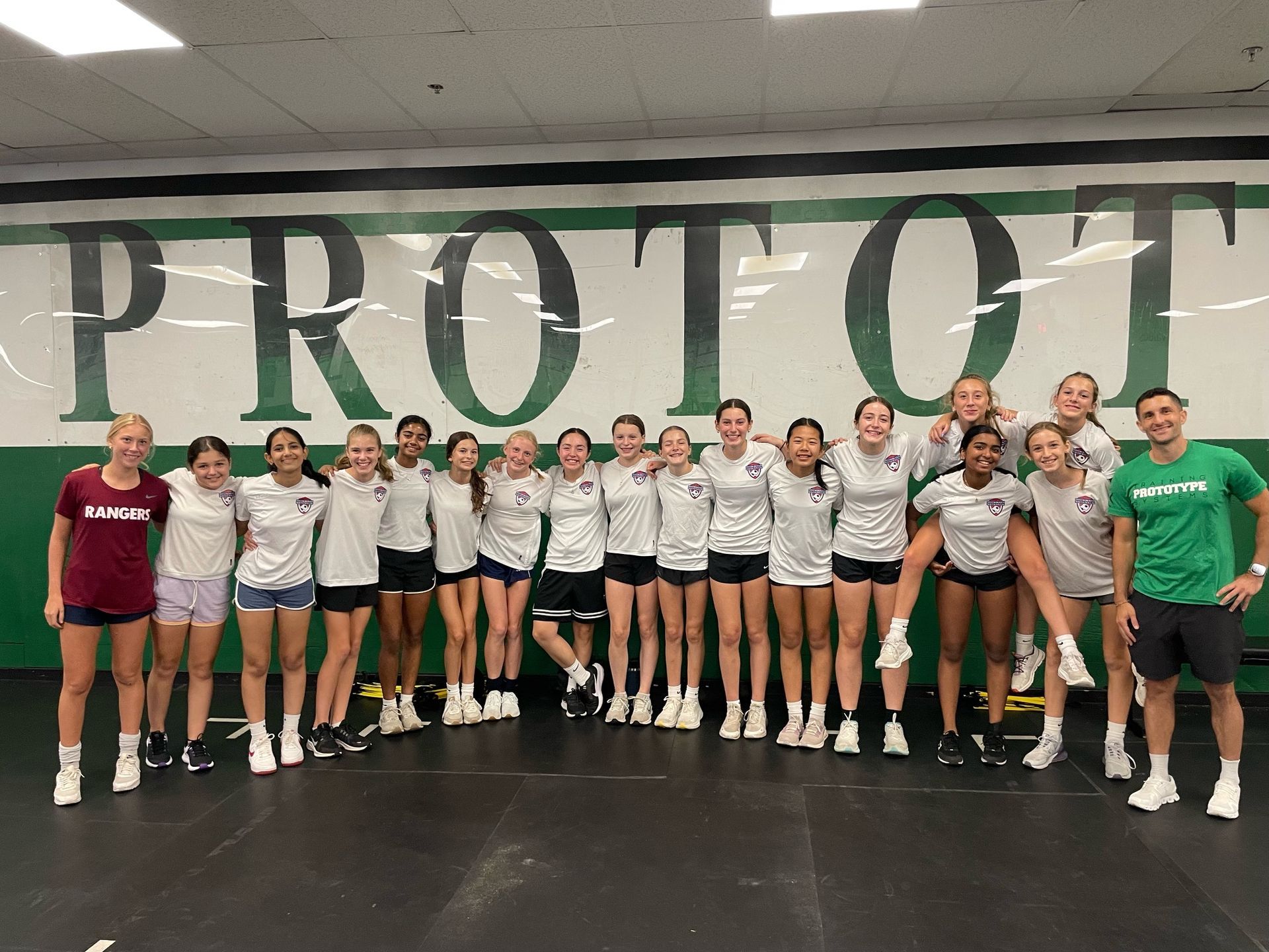 Group of athletes posing indoors in front of a large “PROT” wall mural, wearing team shirts and shorts