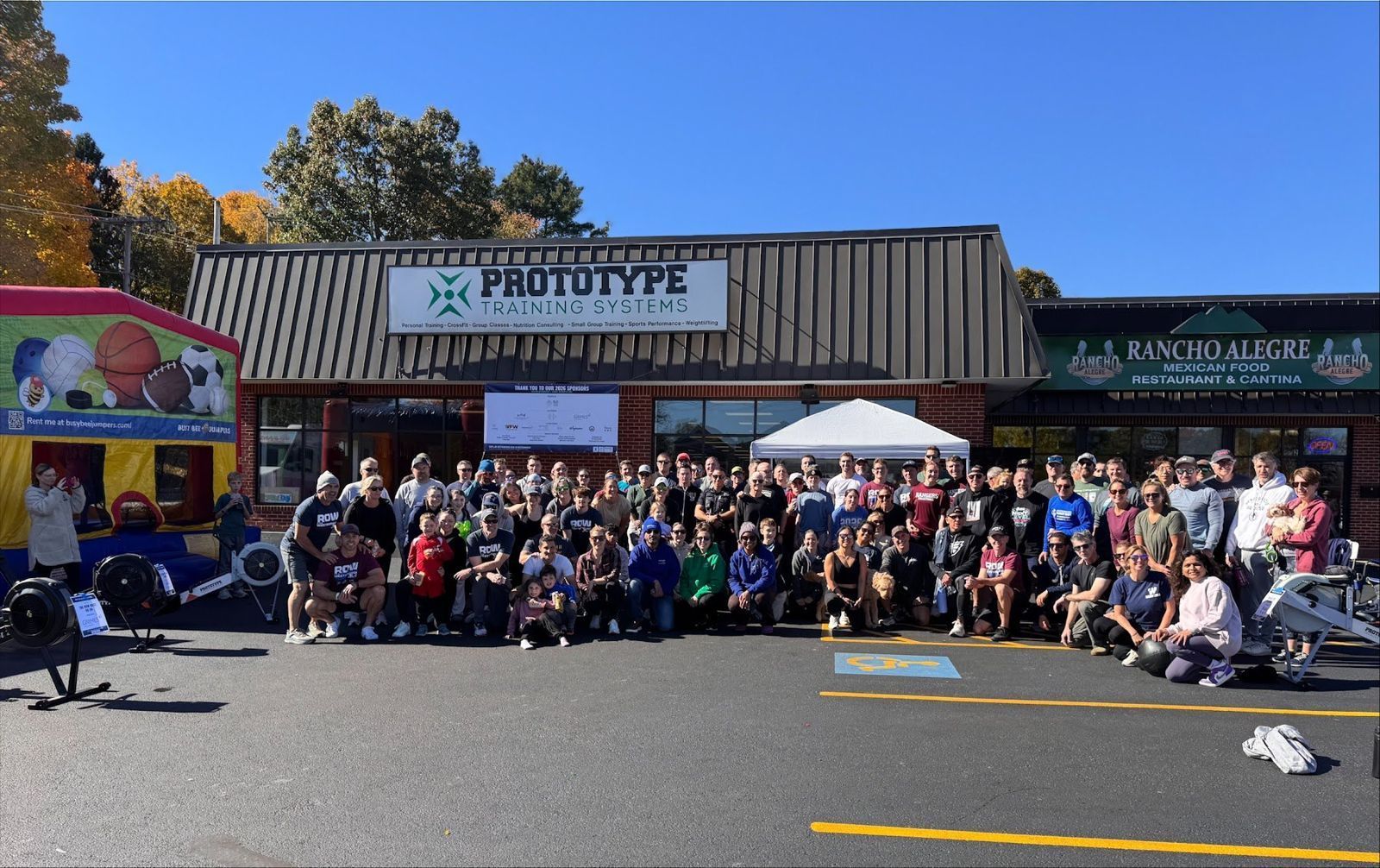 Big group photo of adult rowers and families in front of Prototype Training Systems