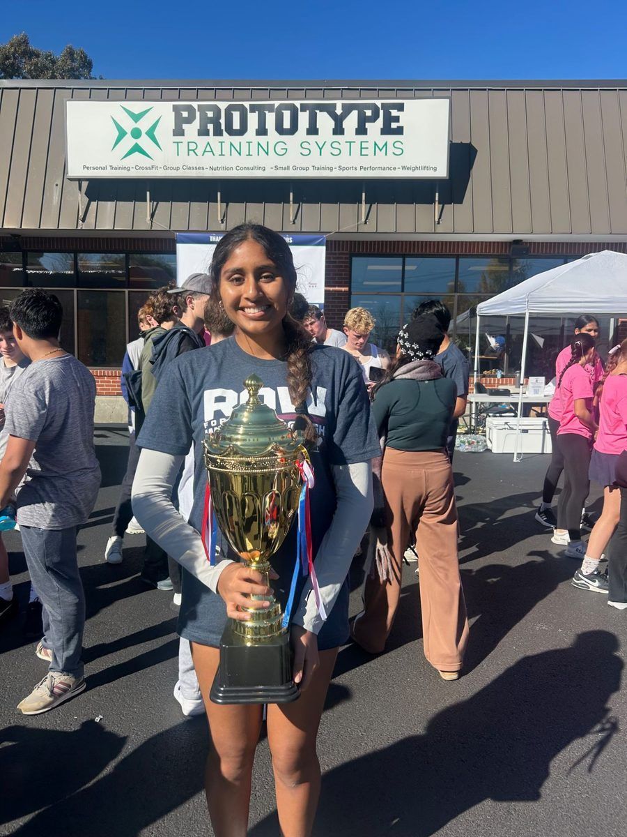 Maahi Srivastava holding the top student fundraiser trophy in front of Prototype Training Systems