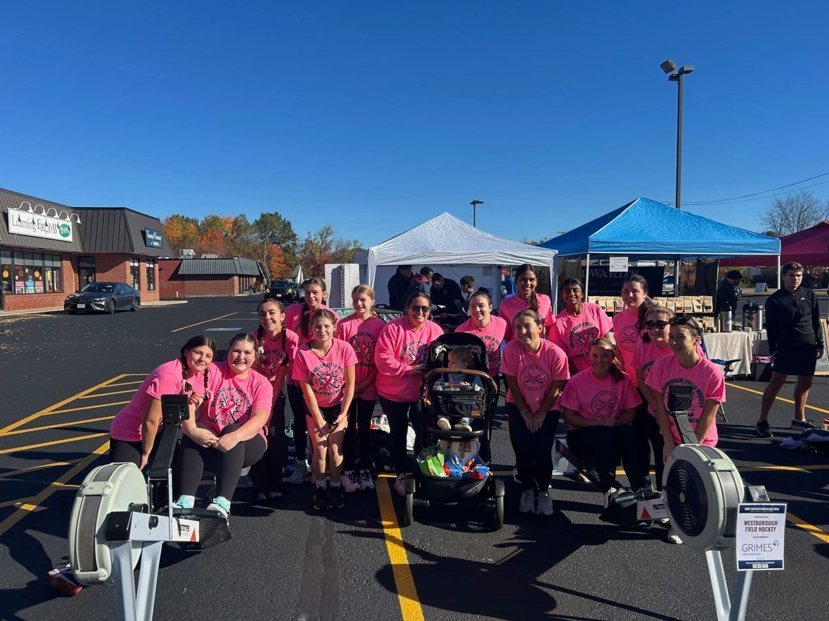 Westborough Field Hockey team in pink shirts gathered around two rowing machines