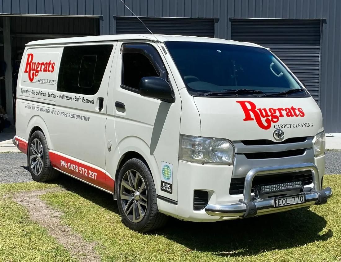 White commercial van with red logos parked on grass in front of black garage doors — Rugrats Carpet Cleaning Service In Old Bar, NSW