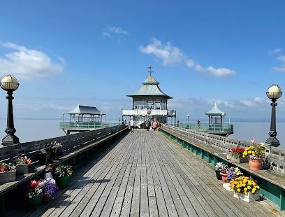 A wooden pier with a pagoda at the end, on a sunny day. Flowers line the sides.
