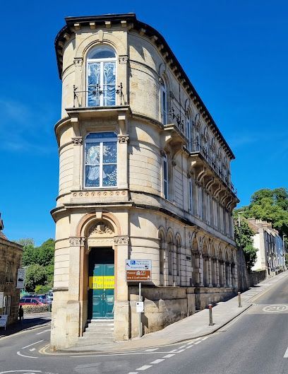 Beige building on a corner lot with curved side and arched entry. Blue sky, sunny day.