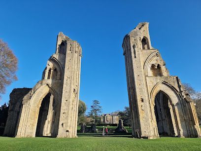 Two crumbling stone towers stand in a grassy field under a clear blue sky, ruins of an abbey.