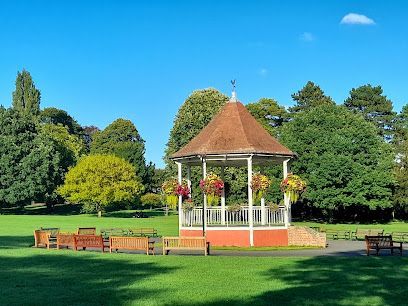 Bandstand in a park, surrounded by green grass and trees, sunny day.