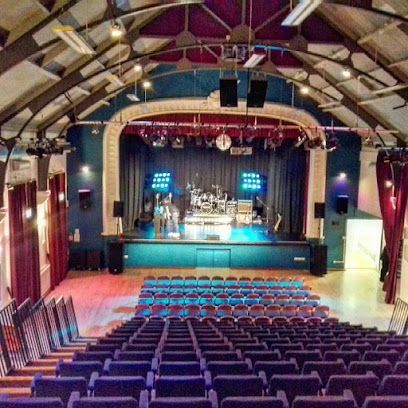 An auditorium with a stage, band, and blue seating. Purple and blue color scheme.